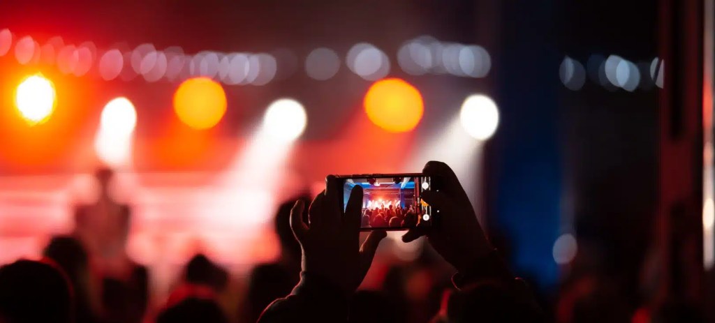 Pessoa filmando um show com smartphone em ambiente de evento