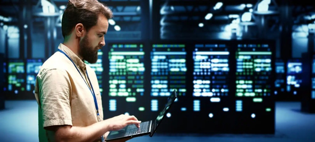 Especialista trabalhando em notebook diante de servidores de um data center